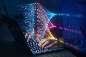 A person types on a laptop with digital data streams visualized in colorful, flowing particle lines emanating from the screen.